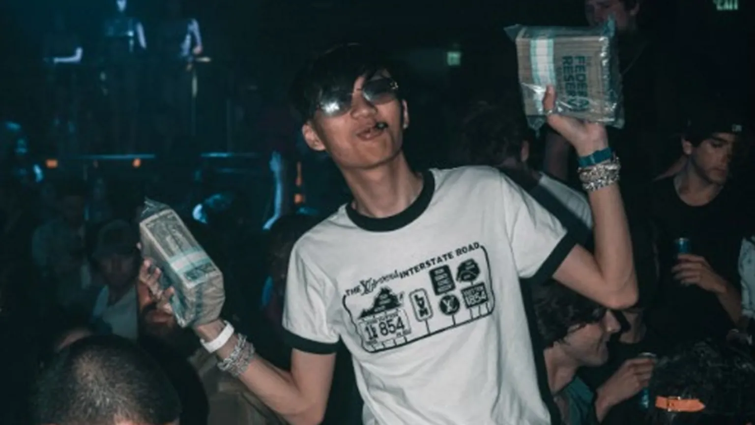 US Department of Justice Malone Lam wears a T-shirt and holds up stacks of cash in a nightclub